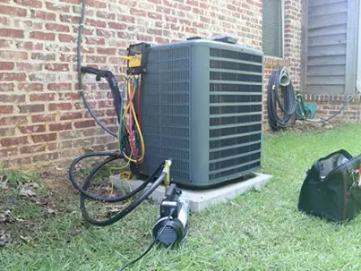 An outdoor AC unit is being serviced next to a brick house