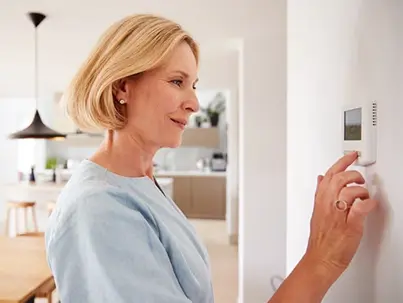 A smiling woman adjusts a digital thermostat on a white wall