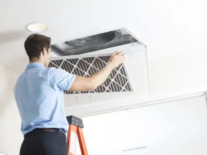 A technician on a ladder replaces an air filter in a ceiling vent