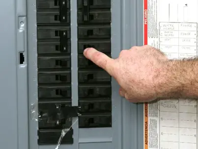 A person's hand points to a circuit breaker inside an electrical panel