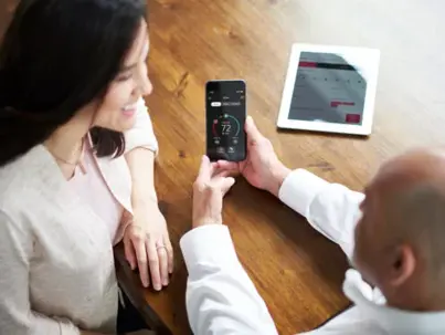 Two people view a smartphone app showing temperature settings for energy management