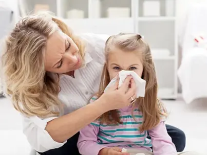 A caring woman gently assists a young girl in blowing her nose with a tissue