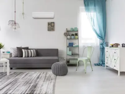 A bright, modern living room featuring a white wall-mounted mini-split air conditioner above a gray sofa