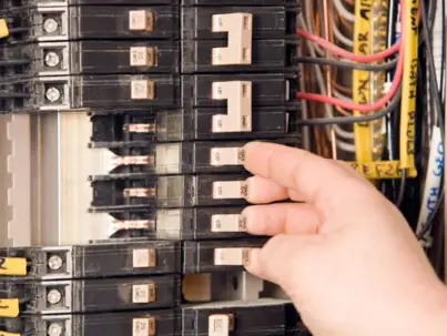 A person's hand adjusts a circuit breaker inside a home electrical panel