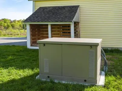 An olive-green standby generator sits on a concrete pad in the grass