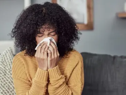 A woman with curly hair uses a tissue to blow her nose
