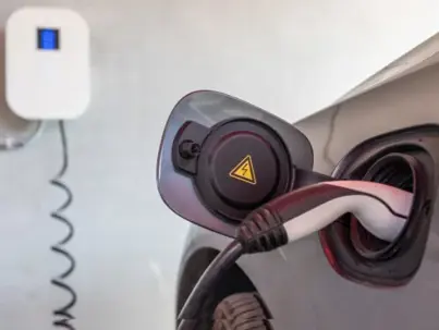 An electric vehicle charges indoors, with a cable connected to its port