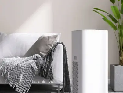 A modern white dehumidifier stands beside a light-colored sofa