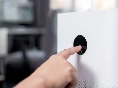 A human hand presses a black control button on a white device
