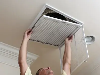 A man is either installing or removing a white washable air filter from a ceiling vent