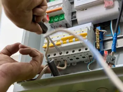 An electrician's hands are busy connecting wires to circuit breakers inside an electrical panel